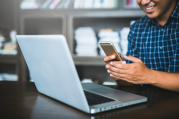 Young casual businessman using laptop, smartphone for working.