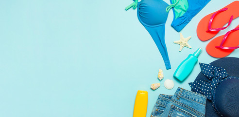 Summer beach sea accessories. Coral flip flops denim shorts female straw hat shells starfish sunscreen bottle body spray on blue background top view flat lay. Summer background. Holiday travel concept