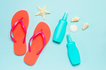 Summer beach sea accessories. Coral flip flops, shells, starfish, yellow sunscreen bottle, body spray on blue background top view flat lay copy space. Summer background Holiday vacation travel concept