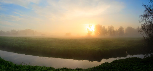 Serene summer panoramic landscape with  forest river and meadow covered by fog at sunrise.