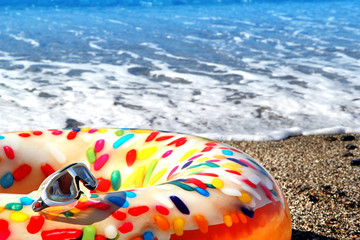 Swimming mask and colorful swim donut on the pebble beach.