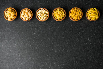 Assortment of different dry pasta types against black background, top view with copy space. Concept...