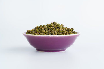 Dried green peppercorns in a violet bowl. White background, high resolution