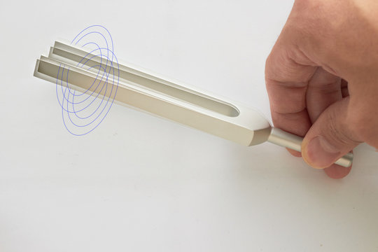Hand holds Tuning fork for ear test of ENT doctor or sound wave maker on isolated  white background with double exposure