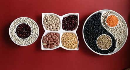 assortment of beans in containers of different shapes on a red background. top view. Flatley.