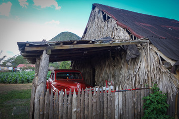 Classic, vintage red car standing below a wooden carport in the famous tourist destination and UNESCO Heritage the Vinales valley, Pinar Del Rio, Cuba