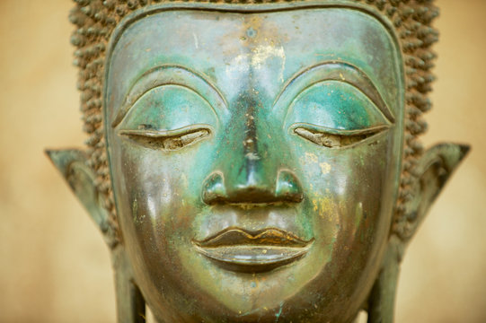 Close up of a face of an ancient copper Buddha statue outside of the Hor Phra Keo temple (former temple of the Emerald Buddha) in Vientiane, Laos.