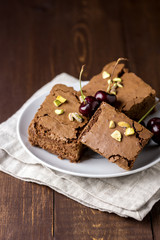 Three Pieces of Tasty Homemade Chocolate Brownies on White Plate Decorated with Cherry and Pistachios Wooden Background Homemade Bakery and Dessert Vertical