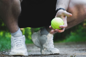 man squatting holds a tennis ball in his hand.