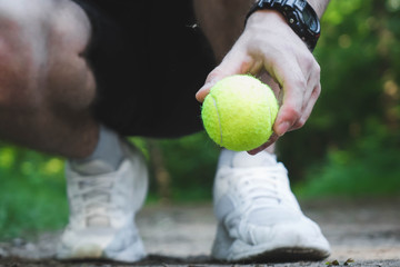 man squatting holds a tennis ball in his hand.