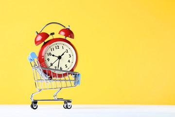 Small shopping cart with alarm clock on yellow background