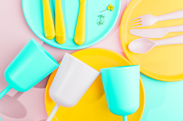 Bright colored plastic picnic utensils. Pink, yellow, blue colors in the bowl. Photo in hard light. Copy space