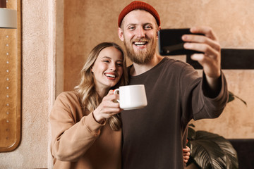 Happy young loving couple in cafe using mobile phone take a selfie.
