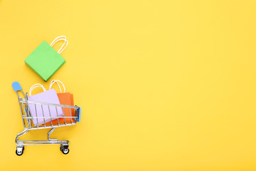 Small metal cart with shopping bags on yellow background