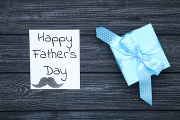 Fototapeta na wymiar Text Happy Fathers Day with gift box on black wooden table