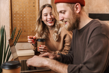 Happy young loving couple in cafe using laptop computer drinking coffee.