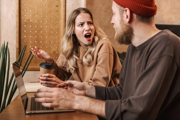 Shocked quarrel young loving couple in cafe using laptop computer drinking coffee.
