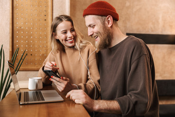 Young loving couple in cafe using laptop computer drinking coffee listening music with earphones.
