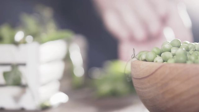 Man's hand breaks a pod of green peas and puts it in a wooden bowl, slow motion. Agricultural concept.
