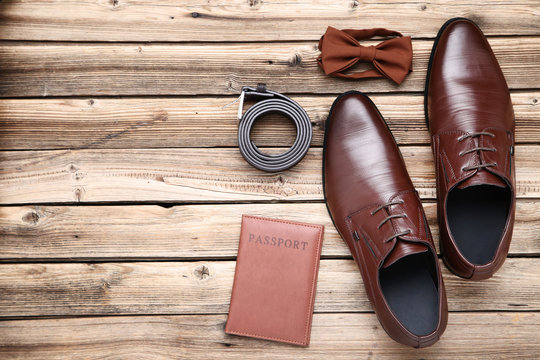 Male leather shoes with passport and accessories on brown wooden table