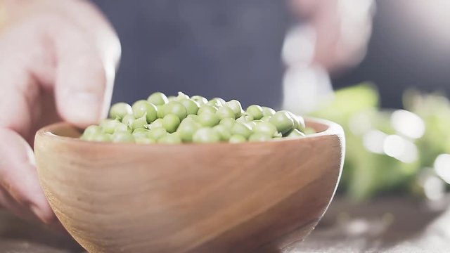 Farmer's hand puts wooden bowl of green peas on table, close-up, slow motion. Agricultural concept. Eco food.