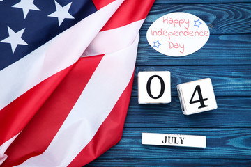 Fototapeta na wymiar Text Happy Independence Day with american flag and cube calendar on blue wooden table