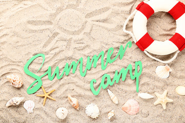 Fototapeta na wymiar Paper text Summer camp with seashells and lifebuoy on beach sand