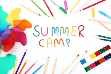 Text Summer camp with school supplies and windmill on white wooden table