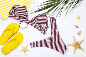 Fashion swimsuit with starfishes and flip flops on white wooden table