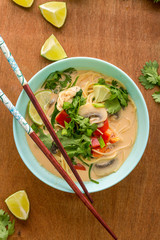 thai chiken ramen in blue bowl on wooden background, top view