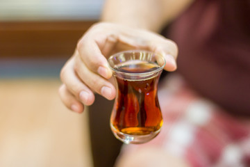 Turkish man holds out black Turkish tea in a traditional glass