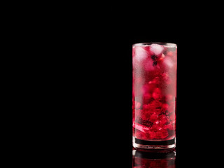 Sweet pomegranate with ice and berry on black background. Delicious summer red lemonade/cold tea.