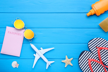 Fashion flip flops with seashells, sunscreen and airplane model on blue wooden table