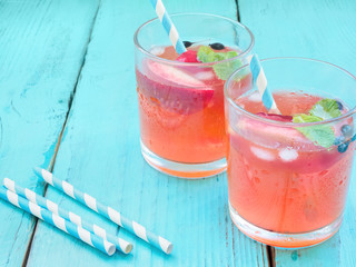 Delicious summer  lemonades with ice,berry, peach and lime on wooden background. Two glass with cold, fresh drink or coctail on blue table