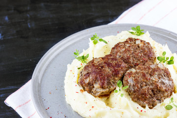 Mashed potatoes and meat balls on a gray plate, decorated with fresh basil