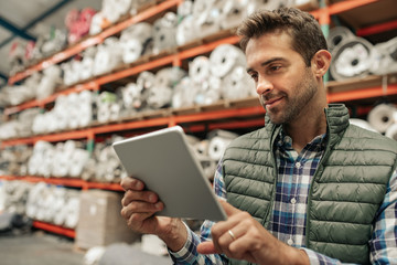 Smiling warehouse worker using a digital tablet to trace stock