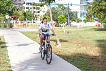 Fashionable young teen girl in shorts and t-shirt rides a bicycle in a summer park