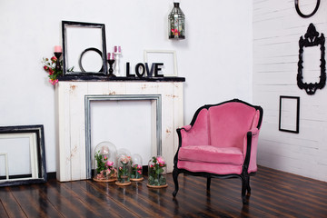 Vintage velor armchair, in a bright room and an artificial fireplace. Interior attic with wooden white walls. Picture frames on the wall. The space where you can put a person. Gothic style room. 