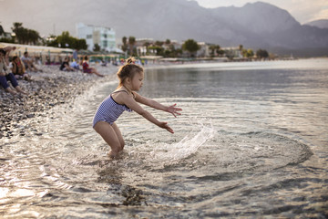 Stylish girl in striped swimsuit playing with sea