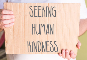 man holding Seeking Human Kindness Sign On Cardboard 