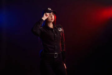 Serious female police officer is posing for the camera against a black background with red and blue backlighting.