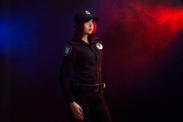 Serious female police officer is posing for the camera against a black background with red and blue...