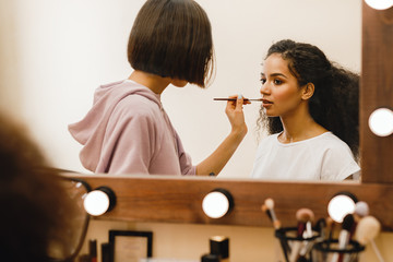 Professional make up artist applying pomade on a model in front of a mirror 