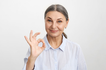 Positive human emotions, reaction, feelings and attitude. Studio shot of beautiful blue eyed woman connecting index finger and thumb in okay gesture, smiling confidently. Everything is perfect