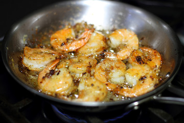 Shrimp scampi cooking in butter and garlic in a stainless steel skillet on the stove.