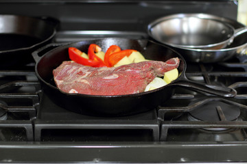 Sirloin tritip steak in a cast iron pan with potatoes and onions on the stove top.
