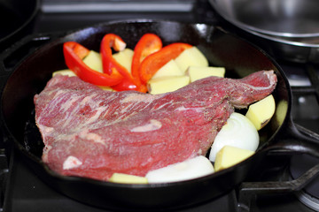 Sirloin tritip steak in a cast iron pan with potatoes and onions on the stove top.
