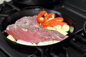 Sirloin tritip steak in a cast iron pan with potatoes and onions on the stove top.