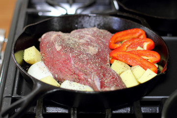 Sirloin tritip steak in a cast iron pan with potatoes and onions on the stove top.