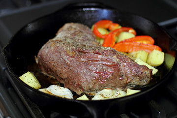 Sirloin tritip steak in a cast iron pan with potatoes and onions on the stove top.